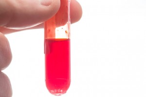 Close up of hand holding vial of blood on white background